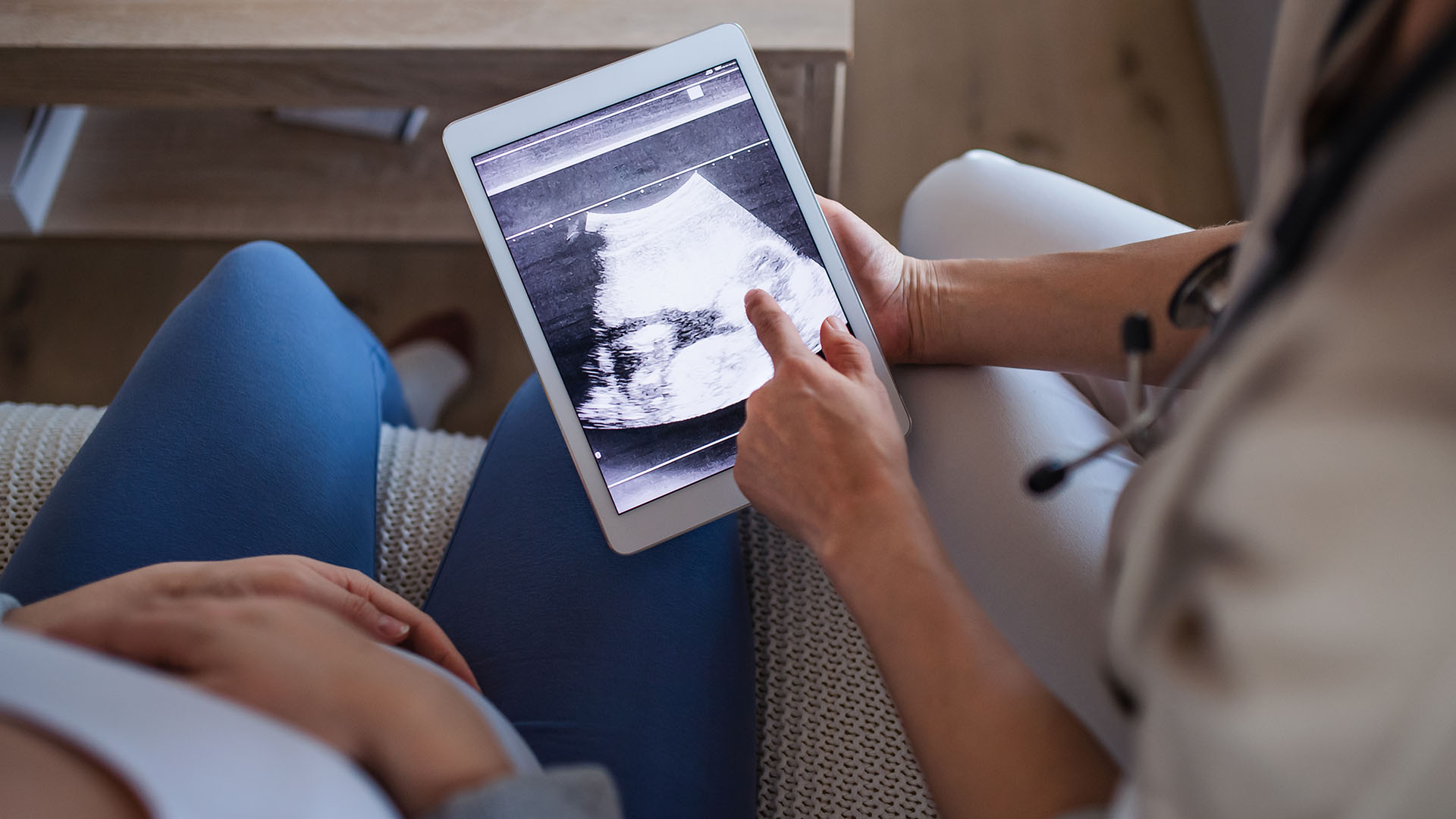 Unrecognizable healthcare worker with ultrasound on tablet and pregnant woman.